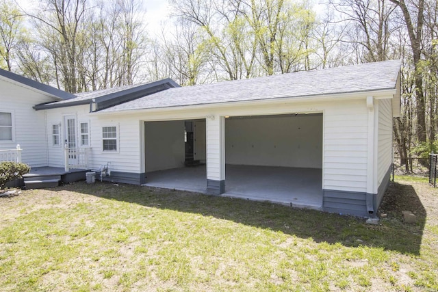 back of house with a garage, a wooden deck, a yard, and roof with shingles