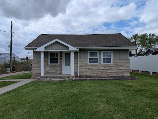 bungalow-style house with roof with shingles, a front yard, fence, and stone siding