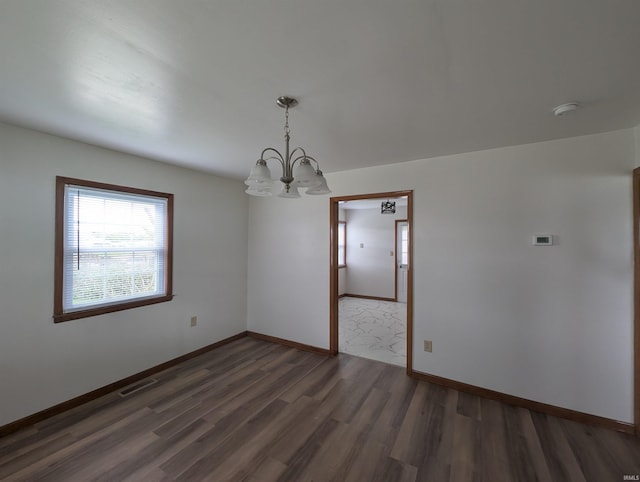 spare room featuring baseboards, a chandelier, wood finished floors, and visible vents