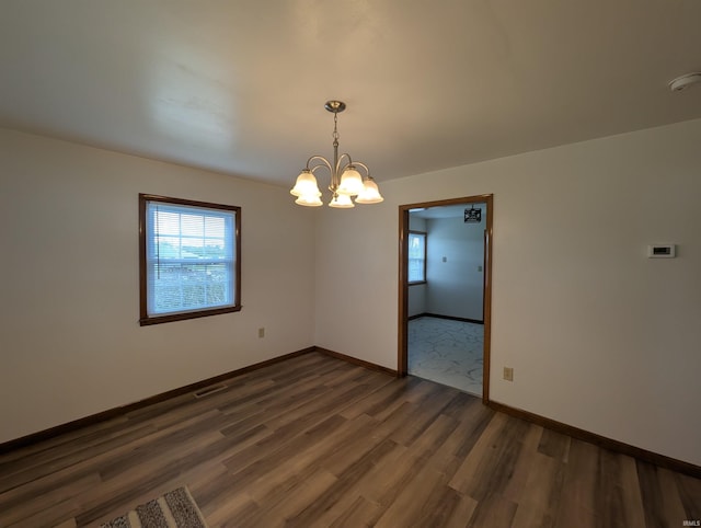 unfurnished room with baseboards, a chandelier, plenty of natural light, and wood finished floors