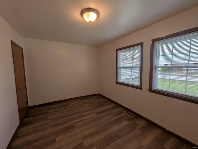 empty room with baseboards, dark wood-style flooring, and visible vents
