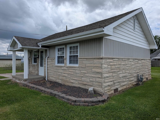 view of front of home with roof with shingles, a front yard, and stone siding