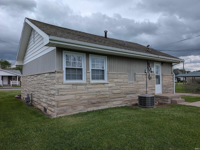 rear view of house featuring a lawn, central AC unit, and stone siding