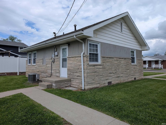 bungalow with fence, a front yard, central AC, and stone siding