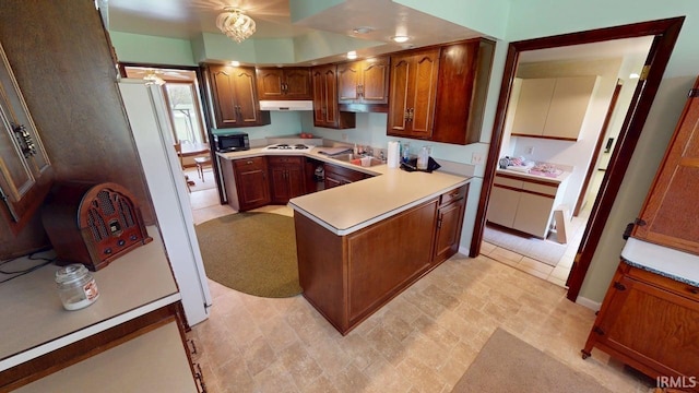 kitchen with brown cabinets, light countertops, a peninsula, under cabinet range hood, and white appliances