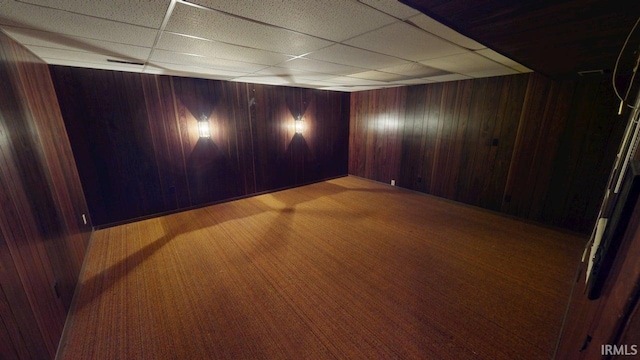 carpeted spare room with visible vents, a paneled ceiling, and wooden walls