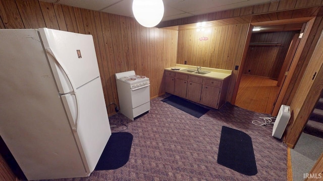 interior space with freestanding refrigerator, wood walls, dark carpet, a sink, and range