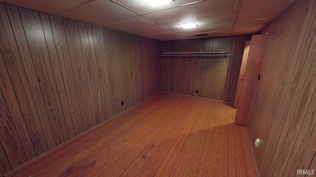 finished basement with wood walls, a drop ceiling, and carpet