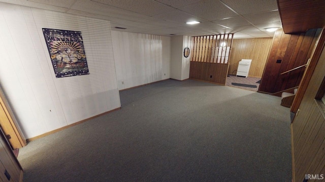 interior space featuring carpet floors, baseboards, wood walls, and a drop ceiling