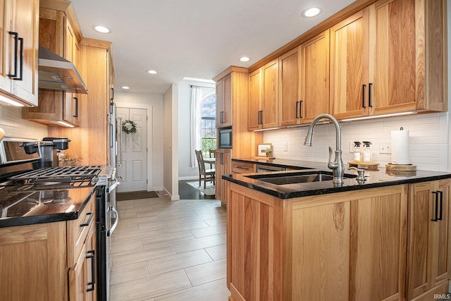 kitchen featuring stainless steel gas range, wall chimney range hood, a sink, baseboards, and tasteful backsplash