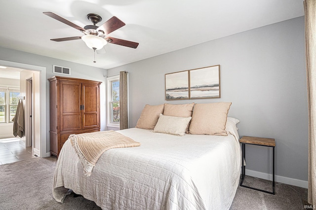 bedroom featuring a ceiling fan, light colored carpet, visible vents, baseboards, and ensuite bathroom