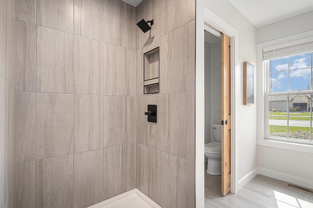 bathroom featuring baseboards, a tile shower, toilet, and visible vents