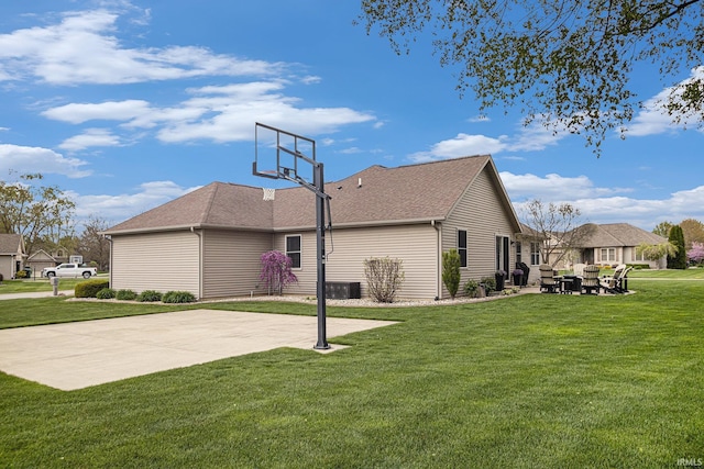view of side of property with basketball hoop, a yard, a patio area, and roof with shingles