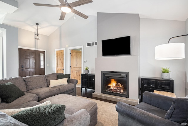 carpeted living room featuring a ceiling fan, high vaulted ceiling, visible vents, and a lit fireplace