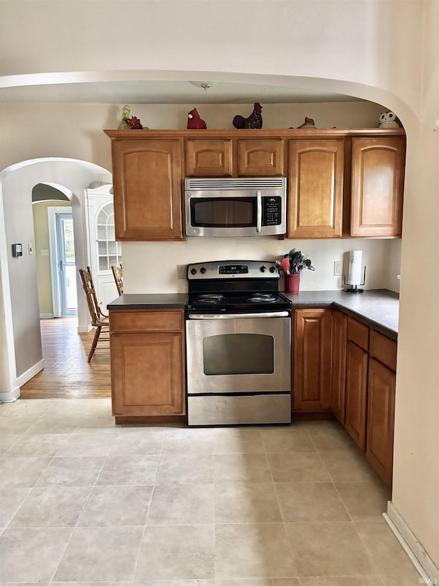 705 Lehman St, Berne, IN 46711 - kitchen featuring arched walkways, appliances with stainless steel finishes, light tile patterned floors, and brown cabinets
