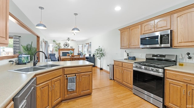 kitchen featuring appliances with stainless steel finishes, a sink, light wood finished floors, light countertops, and a ceiling fan