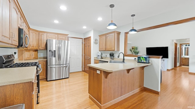 kitchen featuring a peninsula, light wood-style floors, a kitchen breakfast bar, a sink, and stainless steel appliances
