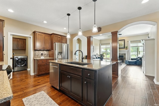 kitchen featuring washer / dryer, a sink, stainless steel appliances, decorative columns, and arched walkways