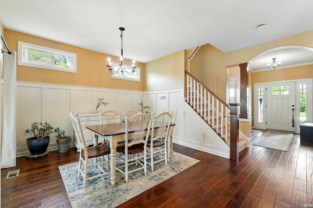 dining room featuring a chandelier, a decorative wall, arched walkways, stairway, and a wainscoted wall