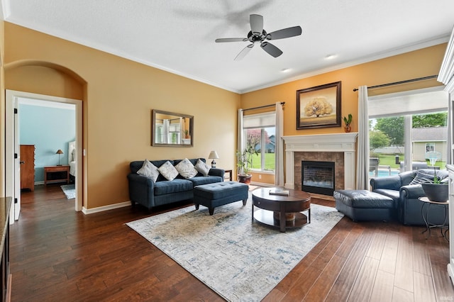 living area featuring a fireplace, a ceiling fan, dark wood finished floors, healthy amount of natural light, and ornamental molding