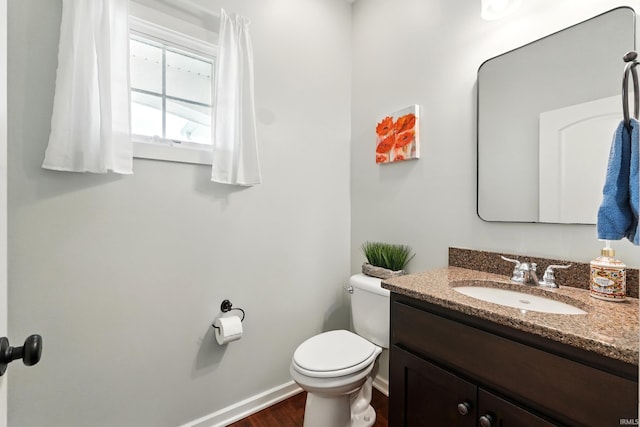 bathroom with toilet, vanity, baseboards, and wood finished floors