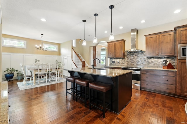 kitchen with wall chimney range hood, stainless steel appliances, a sink, a decorative wall, and decorative backsplash