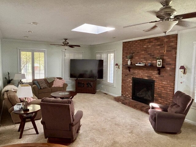 carpeted living room with ceiling fan, a brick fireplace, crown molding, and a skylight