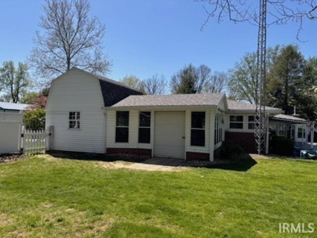 rear view of house featuring a lawn, roof with shingles, and fence