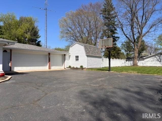 view of side of home with a gambrel roof, an outdoor structure, a garage, and fence
