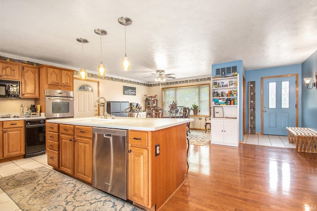 kitchen with stainless steel appliances, a sink, brown cabinets, light countertops, and an island with sink