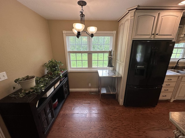 kitchen with a sink, decorative light fixtures, dark wood finished floors, black fridge, and baseboards