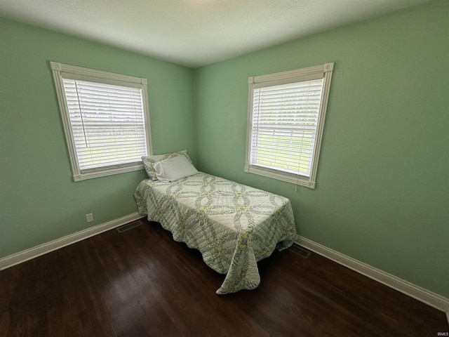 bedroom with dark wood finished floors, baseboards, and multiple windows