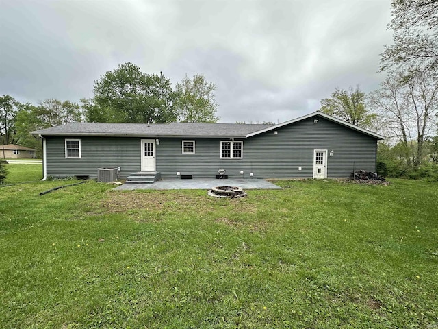 back of property with central AC unit, a patio area, a fire pit, and a lawn