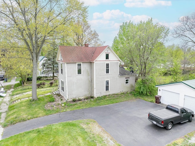 view of side of property featuring a garage, a chimney, a lawn, a shingled roof, and an outdoor structure