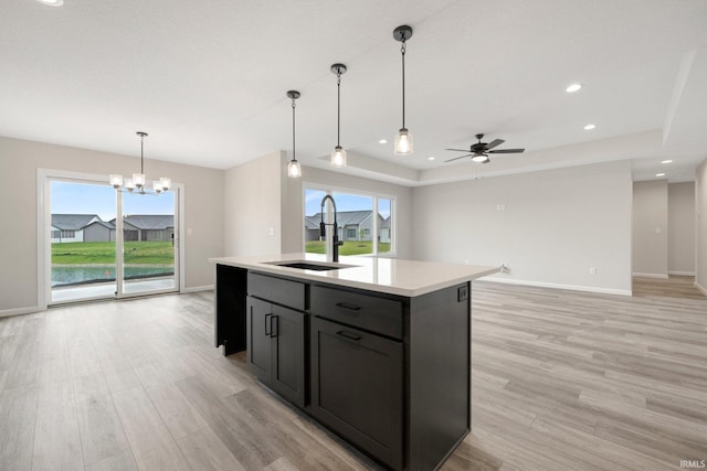 kitchen featuring light countertops, light wood finished floors, a sink, and ceiling fan with notable chandelier