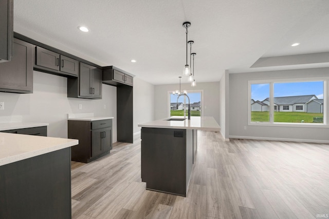 kitchen featuring a sink, pendant lighting, a notable chandelier, a kitchen island with sink, and light wood-type flooring