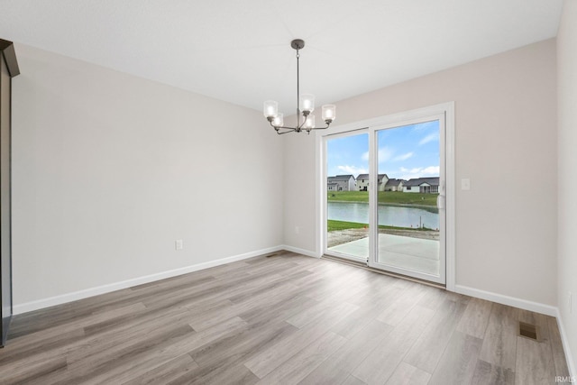 unfurnished dining area with baseboards, visible vents, a water view, a notable chandelier, and light wood-style floors