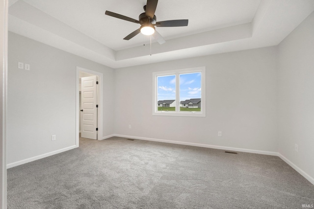 empty room with a tray ceiling, ceiling fan, carpet flooring, and baseboards