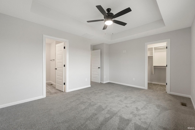 unfurnished bedroom with visible vents, carpet floors, a tray ceiling, a walk in closet, and baseboards