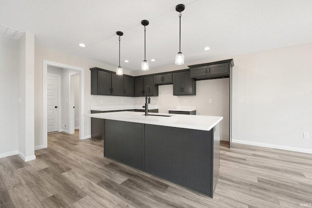kitchen with a sink, a kitchen island with sink, light countertops, baseboards, and light wood-style floors