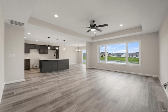 unfurnished living room with baseboards, light wood-style flooring, visible vents, and ceiling fan with notable chandelier