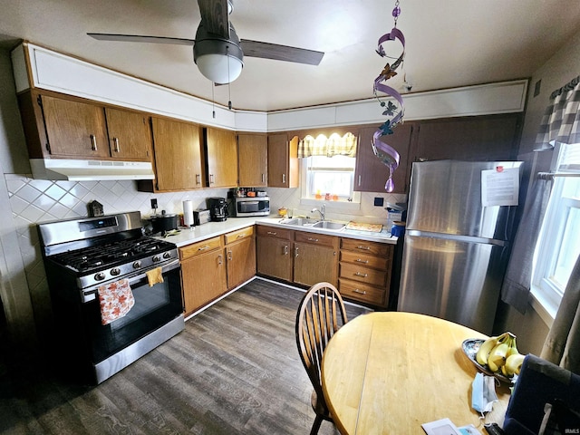kitchen with a sink, stainless steel appliances, dark wood-type flooring, under cabinet range hood, and backsplash