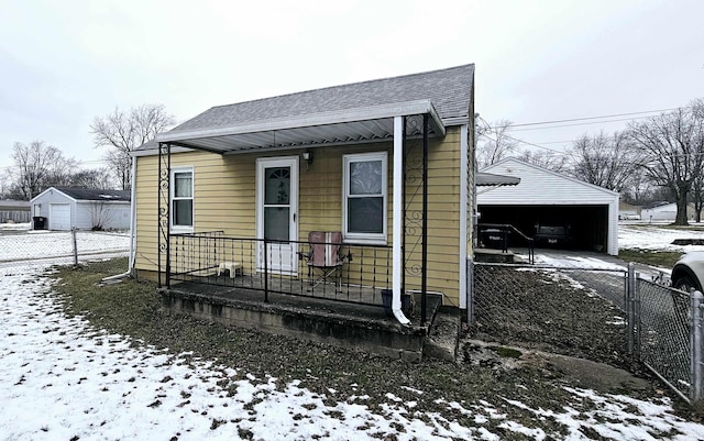 bungalow-style house with roof with shingles, a detached garage, fence, and an outbuilding
