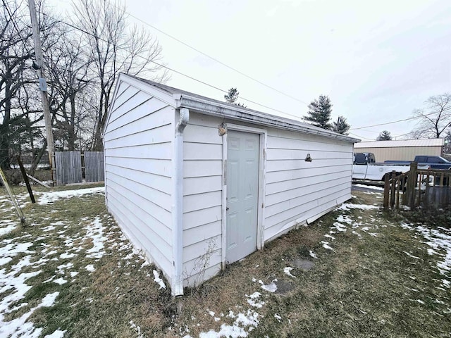 snow covered structure featuring fence and an outdoor structure