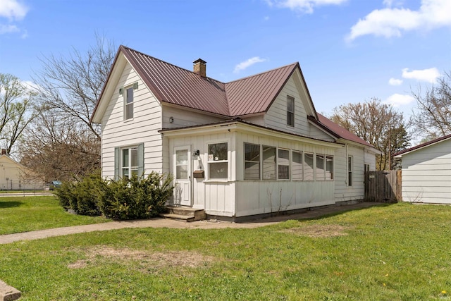 back of house featuring a yard, fence, metal roof, and a chimney
