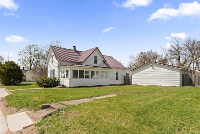 back of house featuring a lawn, a chimney, a sunroom, and metal roof