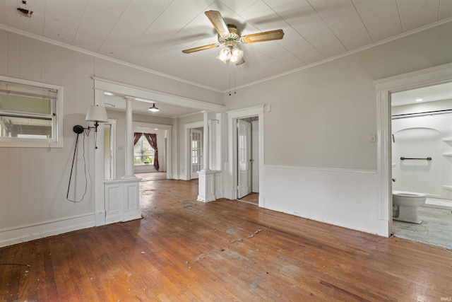 unfurnished living room with hardwood / wood-style flooring, a wainscoted wall, ornamental molding, ornate columns, and a ceiling fan