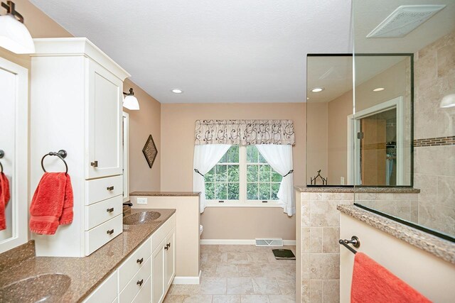 bathroom featuring double vanity, visible vents, baseboards, and a walk in shower