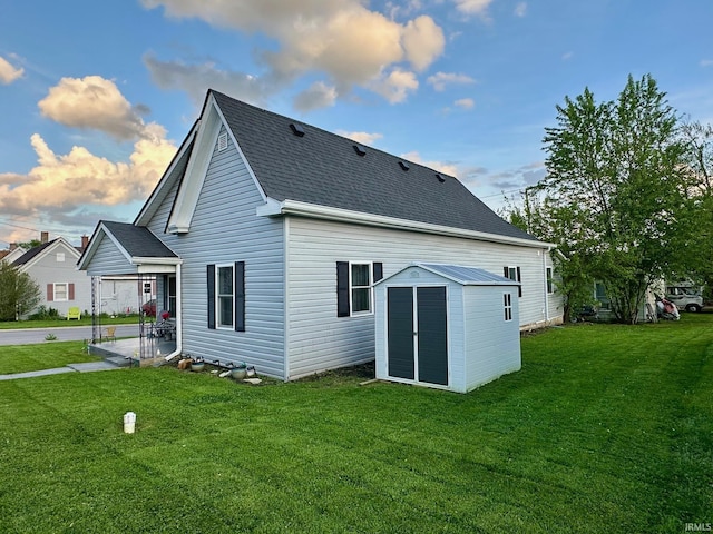 back of property with a lawn, an outbuilding, a shed, a patio area, and roof with shingles