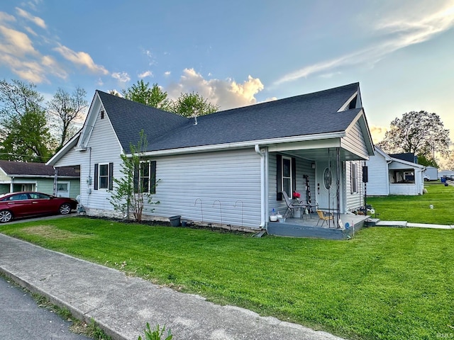 view of side of property with a yard, a shingled roof, and covered porch